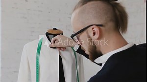 Portrait of a tailor while making a white jacket using the tape measure. Close-up of a professional caucasian tailor taking measures with measuring line on mannequin while crafting a new fashion