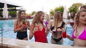 Girls in bikini have pool party with cocktails in swimming pool. Women relaxing clinking glasses with drinks at luxury resort. Female friends in red swimwear dancing, clubbing in a water. Slow motion.