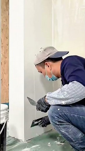 Worker applying smooth joint compound on corner drywall surface manually
