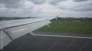 View through airplane window on wing of opening its flaps as it is landing on runway of international airport on cloudy day. Closeup of wing of aircraft flying and landing flaps at airport
