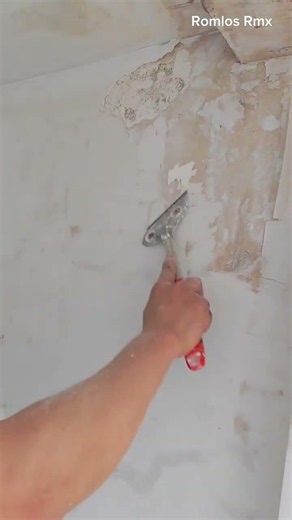 scraping and removing old damaged white paint layer from a concrete wall surface using a manual