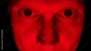 Angry man face under red lighting, showing intense emotions of rage and hostility. Close-up.