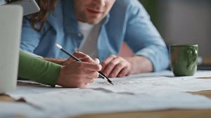 Closeup draftsman hands drawing blueprint planning construction project in office. Creative architects examining plan together. Two engineers discussing building architecture at workplace interior