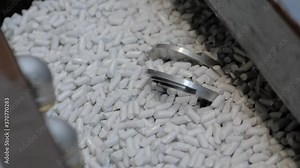 Tumble finishing process at factory - automated trough vibrator machine polishing metal workpieces by abrasive stones - close up. Metalworking, industrial, equipment, technology, manufacturing concept