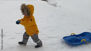 Mother with small child sledding in winter park. Family winter activities outdoors.
