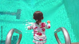 Young Japanese girl jumps into turquoise blue public swimming pool in slow motion. Blue polka dot shirt, blue swimwear. Stock Video