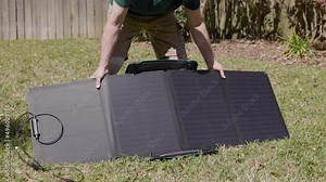 A homeowner unfolding and setting up small portable solar panels in his backyard on a bright sunny day.