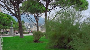 YALTA, RUSSIA - NOVEMBER 18, 2020: Park by the sea with green trees and walking people. Park by the sea with green trees and walking people. Monument on a green lawn against a brown sky mountains