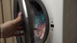Women's hands put clothes in a modern washing machine. The girl carefully cleans clothes with detergent, washing powder, rinse aid in the laundry room. Cleanliness, hygiene, bathroom.