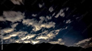 Night time-lapse of the stars moving over the mountain with the clouds moving in the opposite direction