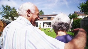 Loving senior couple embrace as they watch their family play in the garden