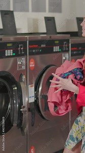 Happy blond woman dance puts the laundry into the washing machine from the basket listening music in laundry room. Housewife fun domestic housework washer routine indoor. Slow motion