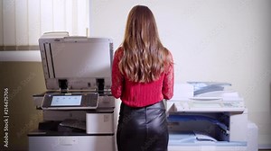 Girl printing in the office. Young beautiful woman making copies of files in the copy machine. Assistant manager working at the office.