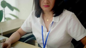 Asian woman working on a laptop in an office setting, focused on her task. The desk features a file organizer, mouse, and documents. A calm, professional work environment is portrayed.