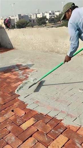 Applying a grey cement layer over a red brick floor with a squeegee to create a smooth surface today