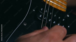 Close-up of the vibrating strings of an electric guitar. A man's hands plectrum strikes the two upper strings. Slow motion. Black guitar