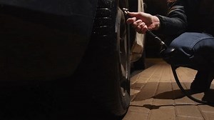 A man checks car flat tire pressure and pumps it up at night at a gas station
