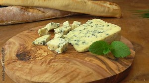 Piece of blue Roquefort cheese lay on a wooden board on a background of french baguettes