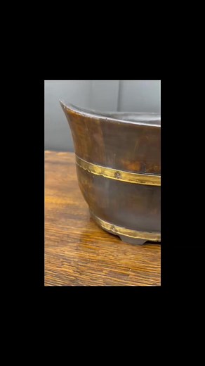 A pair of brass coopered stained pine jardinieres are decorative containers made from brass and stained pine wood. These jardinieres are typically used for displaying plants, flowers, or could also be used for fruit or bread baskets. The brass coopered design refers to the brass bands that encircle the stained pine wood, providing structural support and adding a decorative element. The stained pine wood is treated with a stain or varnish to enhance its natural beauty and protect it from moisture