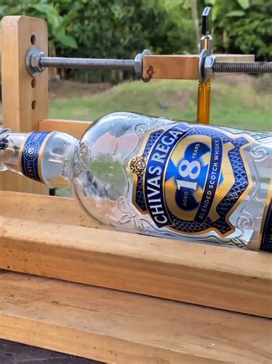 This fascinating DIY setup showcases a creative and satisfying glass-cutting process using a simple handmade wooden machine. The clear glass bottle is carefully secured in a sturdy wooden frame, perfectly aligned to ensure precision and stability. Above the bottle, a sharp cutting tool is attached to an adjustable wooden arm, which is controlled by a threaded rod mechanism. As gentle pressure is applied, the cutter slowly touches the smooth surface of the bottle, creating a precise scoring line 