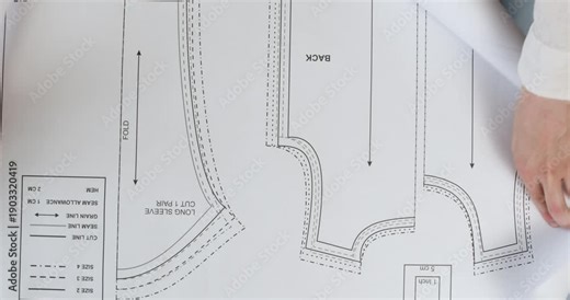 Experienced woman seamstress carefully unfolds detailed paper pattern on wooden table. Skilled female prepares precise scheme for creating clothing element