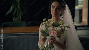 4k young attractive bride with bouquet in modern bridal look with cap sleeves and an illusion neckline top off the column silhouette and sweeping train. Girl in wedding gown seats in restaurant