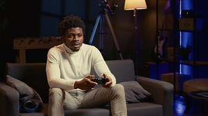 Download Upset BIPOC gamer raging after losing online competitive multiplayer match, playing on gaming console. Man in neon lit living room feeling angry and shouting after being defeated in videogames for free