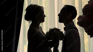 dark outlines of the bride and groom opposite the window. the girl and the young guy are standing sideways, facing each other and talking. wedding