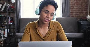 Smart Black teen female wear wireless headphones chat by video call using laptop look at screen discuss training issues with mate teacher. Young woman coach tutor talk to audience before laptop webcam