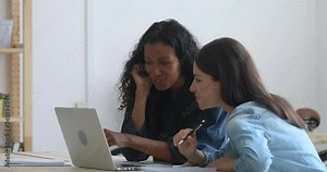 Female caucasian mentor teaching african american intern trainee explaining computer project software at workplace, instructing new worker training online course looking at laptop sit at office desk