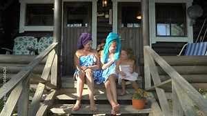 Three female sauna lovers happy together. Young woman, her mature mom and her little daughter having a fun enjoying the silence and fresh air on the porch of a traditional Finnish sauna wearing towels Stock Video