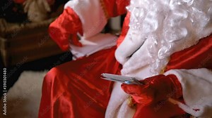 Santa Claus sits in a chair, reads letters that the children sent him and puts them aside. A hands close up. Christmas and New Year. Holiday and celebration. 4K