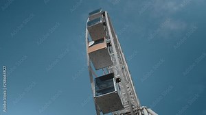A large Ferris wheel rotates against the blue sky in an amusement park. People having fun on the carousel, view from bottom to top.