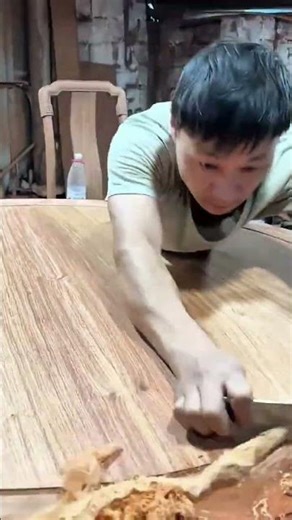Man using hand scraper to smooth a large reddish wood slab
