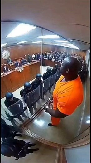 Fixed high-angle CCTV footage captures a spectacular explosion of safety glass in a high-security courtroom. Upon being sentenced to "isolation in a glass box," the Giant Prisoner screams "I HATE GLASS!" and delivers a single massive backhand punch to the partition. The entire 20-foot wall vaporizes into millions of glittering shards, creating a shockwave that knocks down 20 nearby SWAT officers as the giant steps calmly through the newly created opening. Follow FearFeed USA for more raw surveil