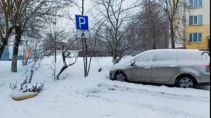 A passenger car is parked near a parking sign for the disabled in winter during snowfall. Copy space for text