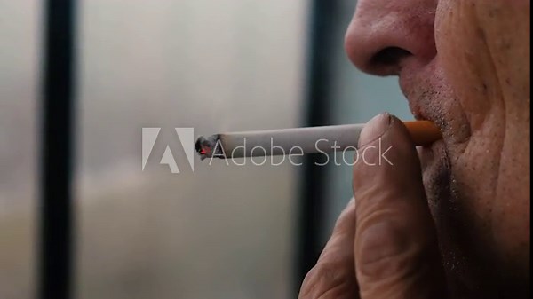 Close-up of a wrinkled old man smoking a cigarette. A pensioner smokes alone on the balcony. The concept of bad habits in old age.