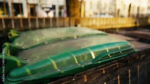 A green trash can sits on top of a wood box next to a building