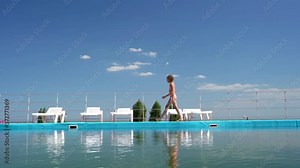 teenage girl in swimsuit goes along pool background sky