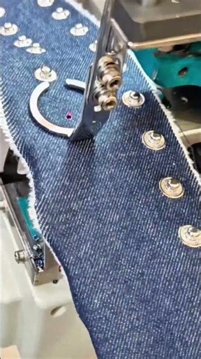 attaching silver metal snap buttons onto blue denim fabric using an industrial press machine now