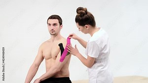 The doctor glues a special treatment tape to mail shoulder. Physiotherapist sticks kinesio tapes to the shoulder of patient, kinesiology taping, kinesiological therapy, athlete are recovering after Stock Video