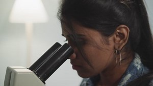 Indian woman with ponytail looks at new types of bacteria through microscope. Student learns to use professional equipment in laboratory closeup