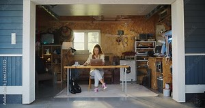 Hispanic Female Software Developer Coding On Laptop Computer In Garage At Home. Focused Young Woman Working On Innovative Online Service Startup. Digital Entrepreneur Starting Company Concept.