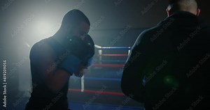 Dynamic shot of young male boxer training with personal coach, fighting on boxing ring. Two athletes practicing punches together in gym.