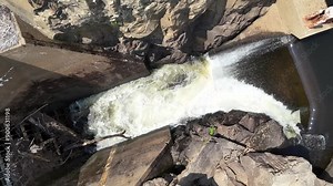 Water rushing into a spillway above a concrete dam - Top down aerial drone shot rising up. Filmed in Northern USA.