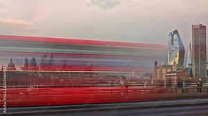 Sunset Time-Lapse in London with the view of the City of London skyscrapers with long shutter in the blue hour. View from the Waterloo Bridge, Red Buses and cars passing by in the foreground.