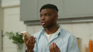 Serious African American male ethnic guy man record voice mail audio message voicemail talk mobile phone loudspeaker recording answer social media smartphone talking loud cellphone microphone at home