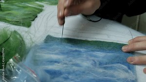 Children work with dry felt. Needle for making paintings from wool. Filling of a blue felt pattern on a white fabric basis. Handmade craft.