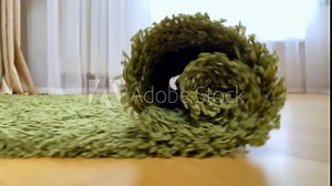 Close up of Rolling out carpet on wooden floor in apartment. Concept of moving in new house. Carpet cleaning service