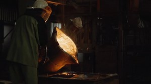 Team of foundry workers pouring glowing molten iron from ladle into molds